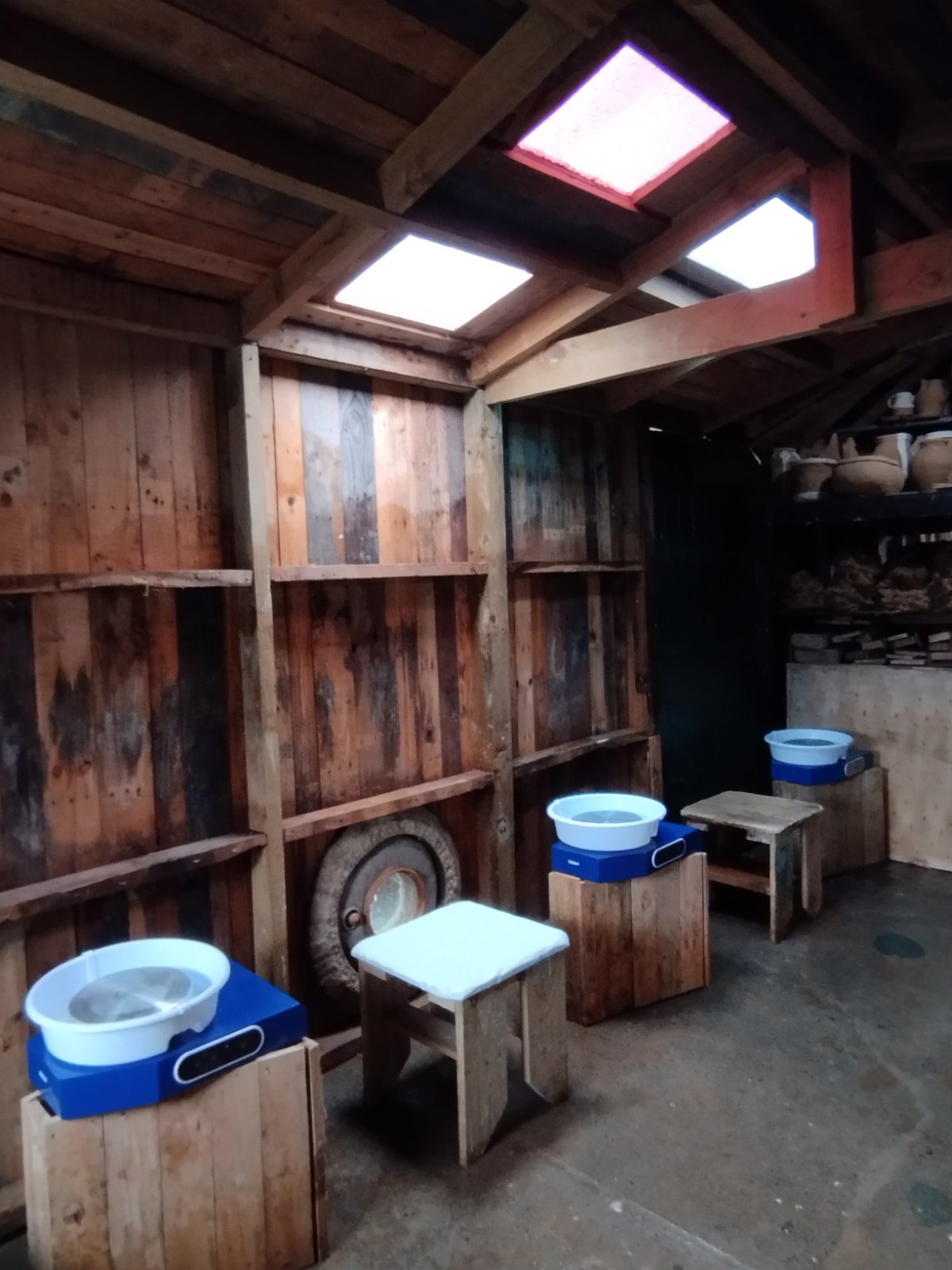 The rustic interior of the Slo Mo Pots studio, showing pottery wheels and stools ready for a small class, set against walls of reclaimed wood.